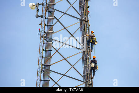 L'entretien de la communication. Deux techniciens d'escalade sur l'antenne de la tour de télécommunications contre fond de ciel bleu Banque D'Images