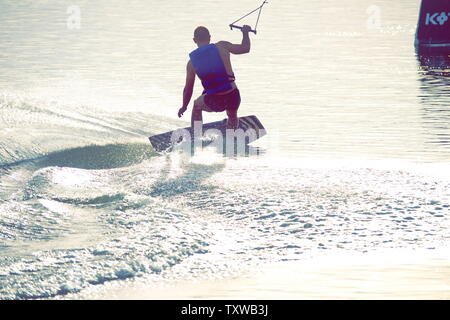 La planche de surf un Ollie saut à coucher du soleil doré. Wakeboarder qualifiés faisant Ollie sauter, projections d'eau tombe dans l'appareil photo. Jeune homme équitation c Banque D'Images