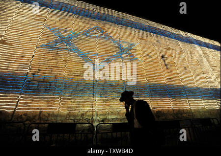 Un homme juif ultra-orthodoxes parle sur son téléphone cellulaire sous un drapeau israélien faite de lumières sur le mur de la vieille ville de Jérusalem le jour de l'indépendance de l'Israël, le 9 mai 2011. Les Israéliens célèbrent le 63e anniversaire de la naissance de l'état juif. UPI/Debbie Hill Banque D'Images