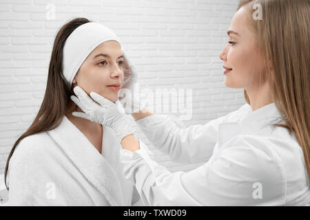 Jeune, jolie femme, centre médical de patients recevant la procédure. Cosmetologist en blouse blanche et gants médicaux en caoutchouc blanc et l'inspection de la face en contact avec le client. Banque D'Images