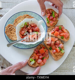 Vue de dessus de mains femme préparer de savoureux hors-d'Italien tomate - bruschetta, sur des tranches de baguette grillées, vue en gros Banque D'Images