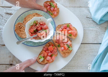 Vue de dessus de mains femme préparer de savoureux hors-d'Italien tomate - bruschetta, sur des tranches de baguette grillées, vue en gros Banque D'Images