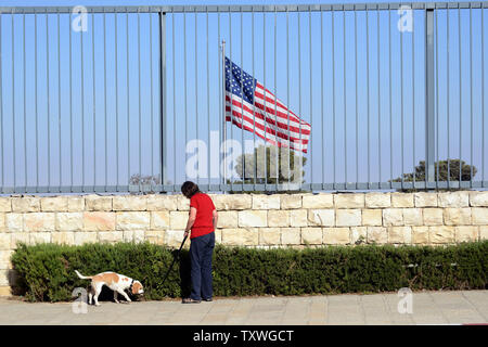 Un Israélien promenades un chien devant un drapeau américain battant derrière une haute clôture qui entoure le bâtiment du consulat général des États-Unis à Jérusalem, Israël, le 3 août 2013. Le Département d'Etat américain a annoncé un plan pour fermer des dizaines d'entre nous, ambassades et consulats au Moyen-Orient et en Afrique du Nord, y compris ceux au Yémen, l'Égypte, l'Irak, l'Arabie saoudite et Israël le dimanche, après l'interception de messages par de hauts membres de l'Al Qaeda discutant des attaques contre des cibles américaines à l'étranger. Les États-Unis ont émis un avertissement aux citoyens américains et aux voyageurs d'éviter les endroits bondés. UPI/Debbie Hill Banque D'Images