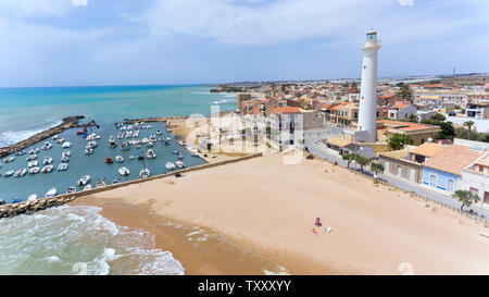 Plage de sable doré avec des eaux peu profondes, petit port avec bateaux, grand blanc phare dans village de pêcheurs sicilien de Punta Secca, ensemble de séries télé l'Insp. Banque D'Images