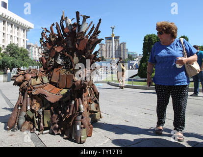 Kiev, Kiev, Ukraine. 25 Juin, 2019. Une femme marche à côté du Trône de fer, au cours de sa présentation à la place de l'Indépendance à Kiev, Ukraine.Les 600 kg d'art par des bénévoles de l'armée de terre Bushtets Denis intitulé ''Trône de fer de l'Est'' est fait de morceaux de réservoir, cartouche ceintures, fragments de missiles, mitrailleuses, obus, soldat des flacons et autres objets militaires qui ont été pris sur la ligne de front avec la Russie sur les séparatistes adossé à l'Est de l'Ukraine. Un prototype d'un célèbre discours du Trône de fer Game of Thrones série TV est un rappel d'un conflit sanglant qui a déjà tué quelque 13 000 peop Banque D'Images