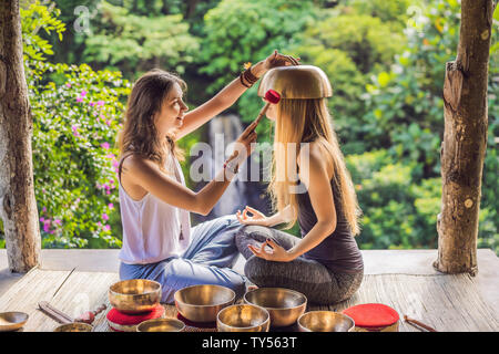 Le Népal en cuivre Bouddha bol chantant au spa beauté. Belle jeune femme faisant la massothérapie singing bowls dans le Spa contre une chute d'eau. Thérapie sonore Banque D'Images