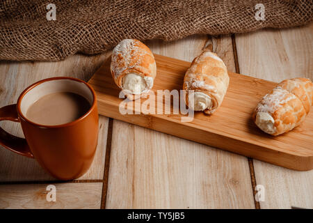 Rouleaux de pâte feuilletée avec de la crème sur un support en bois dans un style rustique Banque D'Images