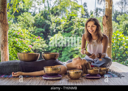 Le Népal en cuivre Bouddha bol chantant au spa beauté. Belle jeune femme faisant la massothérapie singing bowls dans le Spa contre une chute d'eau. Thérapie sonore Banque D'Images