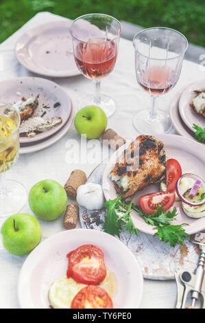 Verres de vin blanc et rose, du poisson grillé, des plaques, légumes, salades et fruits sur la table. Fête de l'été dans l'arrière-cour. Shot verticale Banque D'Images