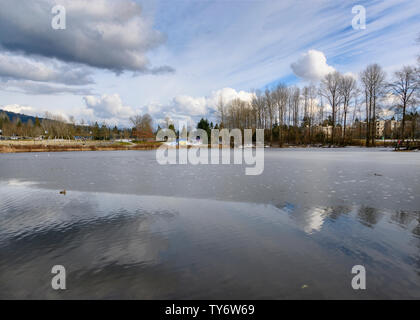 belle scène d'hiver avec lac partiellement gelé, couvert de glace brisante . Bâtiments et arbres en arrière-plan. Nuageux, ciel bleu. Superbe hiver la Banque D'Images