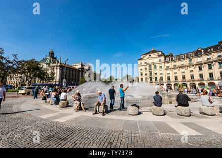 Les touristes visitent la Karlsplatz ou Stachus, grande place, dans le centre de Munich avec une fontaine, en arrière-plan le Palais de Justice (Justizpalast), Allemagne Banque D'Images