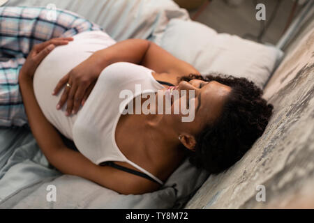 Smiling pregnant woman sur son lit. Banque D'Images