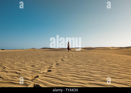 Les jeunes évocateur certain femme marche sur son propre chemin sur le sable du désert avec robe rouge dans l'middlw de dunes sur chaude journée d'été avec ciel bleu clair Banque D'Images