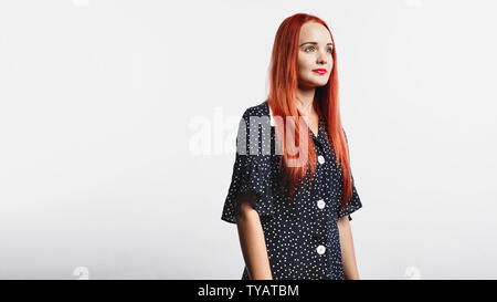 Portrait de jeune femme à la recherche de l'établissement. Femme aux longs cheveux brun rougeâtre standing against white background. Banque D'Images