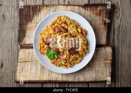 Cuisine orientale. Pilaf ouzbek ou plov du riz et de la viande. Fond rustique en bois. Vue de dessus avec copie espace. Banque D'Images