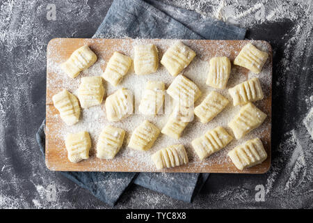Gnocchi de pommes de terre maison crus brut avec de la farine sur une planche à découper. Vue d'en haut. Fond sombre. Banque D'Images