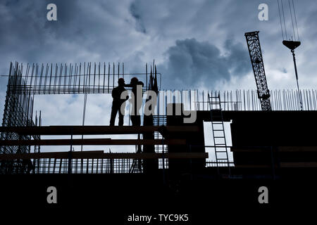 Silhouette de deux travailleurs sur le haut d'un immeuble en construction Banque D'Images