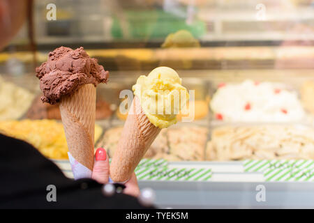 Une femme tient à la main deux tubes de crème glacée, chocolat et mangue, sur l'arrière-plan de la glace du comptoir. Banque D'Images