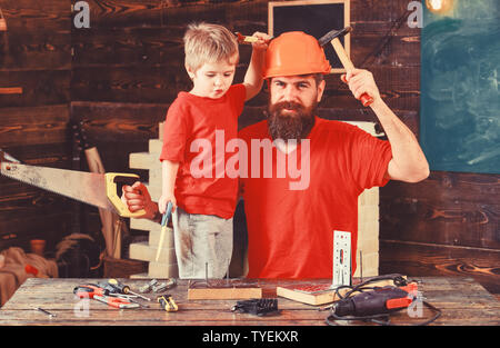 Garçon, joyeux enfant jouet est vu, avoir du plaisir alors que l'artisanat avec papa. Concept de la paternité. Père, parent avec casque de protection à barbe fils d'enseignement d'utiliser des outils différents à l'École Atelier. Banque D'Images