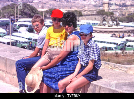 La famille britannique pose pour les vacances photo snap le jour très chaud des années 1980 Malte Maman et trois enfants Valletta gare routière centrale vieux bus verts photo par papa Banque D'Images