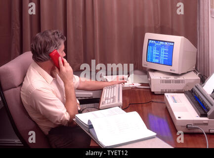 Historique 1988 image d'archive travailleur de bureau homme indépendant assis au bureau travaillant tard à la maison rideaux tirés fermés à l'aide de téléphone fixe rouge Amstrad ordinateur de bureau écran bleu et imprimante archive 1980s la façon dont nous étions WFH en Angleterre Royaume-Uni dans les années 80 Banque D'Images