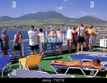 Femme des années 90, les bains de soleil et des couples de garde-corps sur le pont de navire de croisière à faire des photos de Basseterre côte paysage île des Caraïbes de Saint Martin Banque D'Images