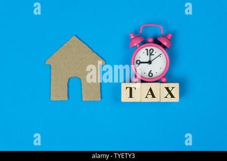 Un concept de taxes foncières. Une petite maison et rose réveil avec du texte sur fond bleu en vue de dessus. Illustre l'importance de la gestion des biens Banque D'Images