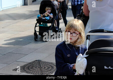 Juin 2019, Cardiff, Pays de Galles. Cute Kids avec leurs parents à l'extérieur St David's Dewi Sant. Fille blonde avec des lunettes, la pram/poussant président Banque D'Images