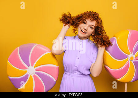 Rousse bouclée femme positive s'amusant sur lollipops arrière-plan. Oui j'aime les bonbons sucrés Banque D'Images