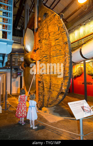 Deux filles / enfants kids kid visiteurs touristes regarder le gouvernail, hélice & du cadre de levage de la mairie à l'intérieur du Musée de l'Arsenal au bateau à vapeur de Brunel à Bristol. Royaume-uni (109) Banque D'Images