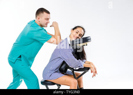 Massage thème et bureau. Costume bleu avec un thérapeute de sexe masculin faisant massage du dos et du cou pour les jeunes femme, femme d'affaires en chemise sur un fauteuil de massage s Banque D'Images