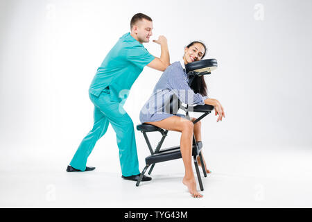 Massage thème et bureau. Costume bleu avec un thérapeute de sexe masculin faisant massage du dos et du cou pour les jeunes femme, femme d'affaires en chemise sur un fauteuil de massage s Banque D'Images