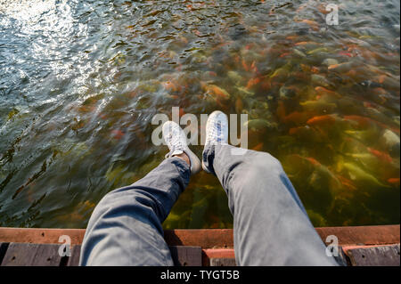 Homme assis de loisirs sur un patio en bois avec koi fish swimming in pond Banque D'Images