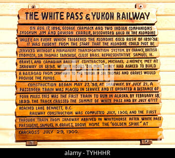 Une piscine panneau en bois donne un bref historique de la remarquable White Pass and Yukon Railway qui a proposé le premier service de train en Alaska, USA, et a été construit à cause de la ruée vers l'or de 1897-1898 au Klondike, dans le Territoire du Yukon du Canada. Le panneau est affiché dans Skagway, en Alaska, où les prospecteurs montait dans le train de monter de niveau de la mer 2 915 pieds (888 mètres) sommet du col White et raccourcir leurs 600 milles (960 kilomètres) voyage à la Goldfields. De nos jours les touristes ride in vintage WP&Y voitures qui retracent l'itinéraire jusqu'au sommet du col White et profiter de paysages à couper le souffle. Banque D'Images