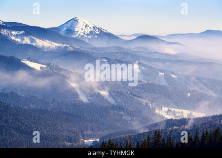 De hautes montagnes avec de l'hiver des pistes de ski resort avec brouillard et les nuages éclairés par la lumière du soir Banque D'Images