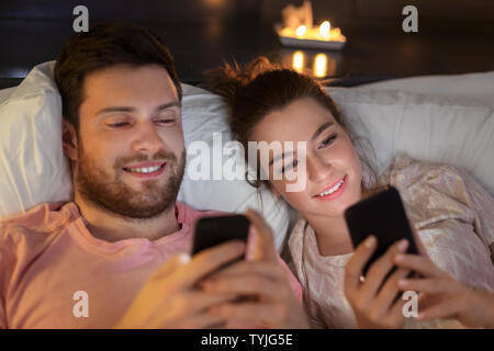 Couple heureux en utilisant les smartphones en lit la nuit Banque D'Images