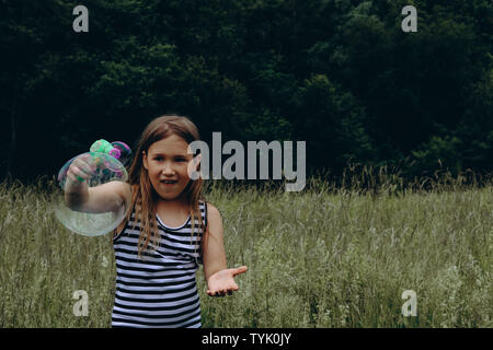 Girl blowing bubbles avec canon à bulles. Jeune enfant jouer dehors. Activités de jour d'été. Heureux, joyeux enfant à l'extérieur. Avoir du plaisir seul. Belle et pittoresque paysage forestier. Paysage pittoresque Banque D'Images