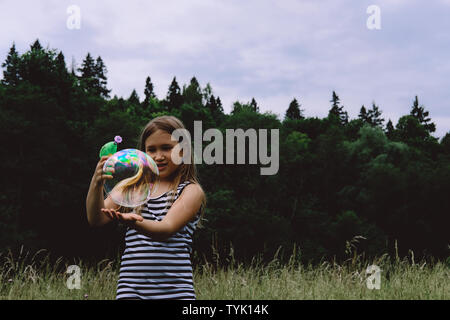 Girl blowing bubbles avec canon à bulles. Jeune enfant jouer dehors. Activités de jour d'été. Heureux, joyeux enfant à l'extérieur. Avoir du plaisir seul. Belle et pittoresque paysage forestier. Paysage pittoresque Banque D'Images