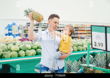 Papa père caucasien dans épicerie holding pineapple et carrying baby fils pendant leurs achats l'achat des fruits frais. Homme parent avec enfant kid choisir Banque D'Images