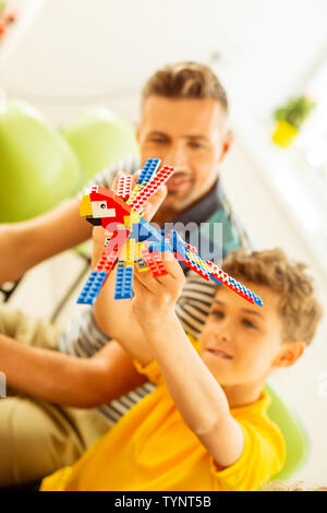 Jouet préféré. Happy cute boy jouant avec un perroquet jouet tout en le construisant lui-même Banque D'Images