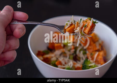 Une bouchée d'une salade de nouilles de patate douce Brocoli sur une fourchette, avec plus de la salade dans le bol ci-dessous Banque D'Images