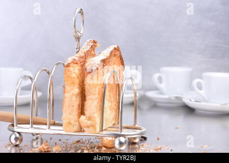 Argenterie ancienne toast rack avec des tranches de pain frais et de tasses de café dans l'arrière-plan, pendant le petit déjeuner Banque D'Images