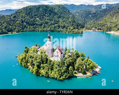 Vue aérienne de l'île de Bled ou Blejski Otok, l'assomption de Marie l'église avec une tour et spire, sur le lac de Bled de montagne pleine de pletna les bateaux, entouré b Banque D'Images