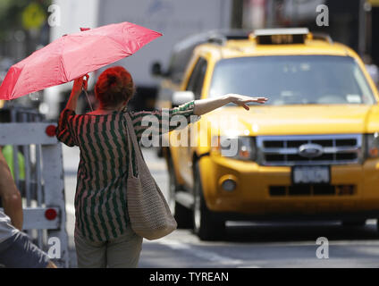 Une femme porte un parapluie pour son bouclier du soleil alors qu'elle salue un taxi dans l'East Village de Manhattan à New York City le 25 juillet 2016. Six décès liés à la chaleur ont été signalées comme des températures dangereusement élevées continuent de brûler certaines parties de l'Est des États-Unis, où la chaleur Avis aux médias demeurent en vigueur lundi. Photo de John Angelillo/UPI Banque D'Images