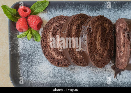 Swiss roll avec de la confiture au chocolat décoré avec des framboises dans une assiette. Des bonbons. Focus sélectif. Banque D'Images