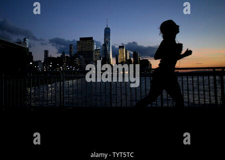 Un jogger s'exécute au coucher du soleil comme en deuil recueillir et attendre pour descendre la piste cyclable en direction de One World Trade Center et le lower Manhattan le long de la West Side Highway participant à une veillée aux chandelles en l'honneur des victimes de la terreur deux jours après jour après un Home Depot chariot claquée par laissant 8 morts et plus d'une douzaine de blessés dans le sud de Manhattan le 2 novembre 2017 à New York. Le suspect en détention, Sayfullo Habibullaevic délibérément, a conduit un camion loué Home Depot sur une longue piste cyclable à proximité du World Trade Center dans le lower Manhattan, tuant huit personnes et sérieusement injurin Banque D'Images