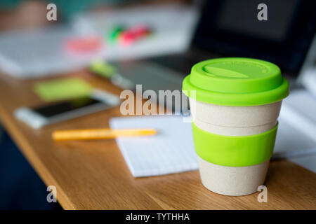 Une tasse de café réutilisable bambou est assis sur une table en bois ainsi que d'autres articles tels que les livres et un ordinateur portable qui suggère c'est un espace d'étude. Banque D'Images