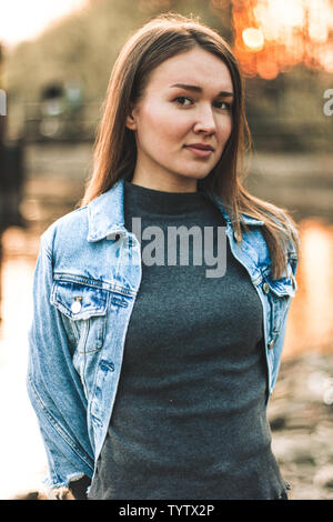 Portrait de la jolie, mince, belle jeune fille blonde caucasienne dans une veste de jeans. Smiling girl bénéficie d'amende contre la météo sunner chaud Banque D'Images