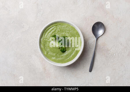 Soupe crème de brocoli avec récipient blanc en béton blanc avec cuillère sur arrière-plan. Concept d'aliments pour bébé. Espace libre pour le texte Banque D'Images