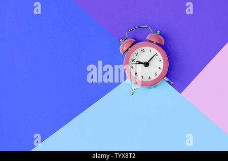 Un petit réveil rose est situé entre les zones de bleu, violet et rose Couleurs. Concept de gestion du temps. Télévision jeter un minimum d'un modèle à copier l'espace. Banque D'Images